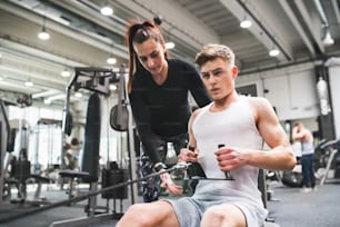 Fit young man in gym with his personal trainer working out on cable weight machine.
