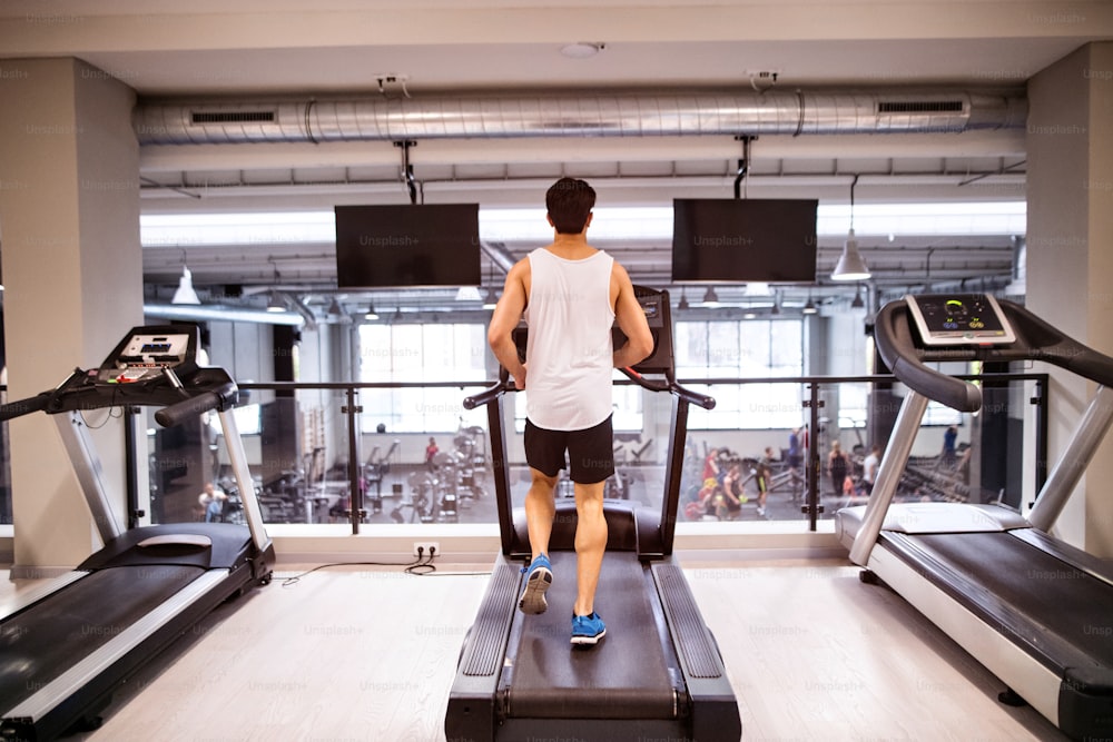 Young hispanic fitness man in sports clothing in gym doing cardio workout, exercising on treadmill. Sport fitness and healthy lifestyle concept. Rear view.