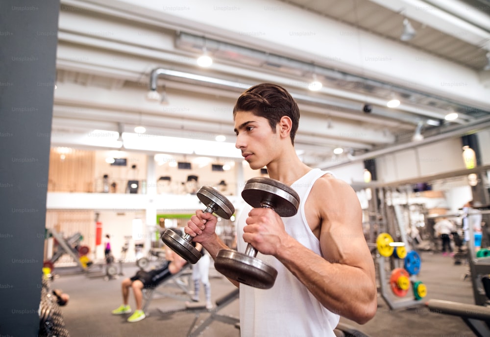 Apuesto joven hispano en el gimnasio haciendo ejercicio con pesas