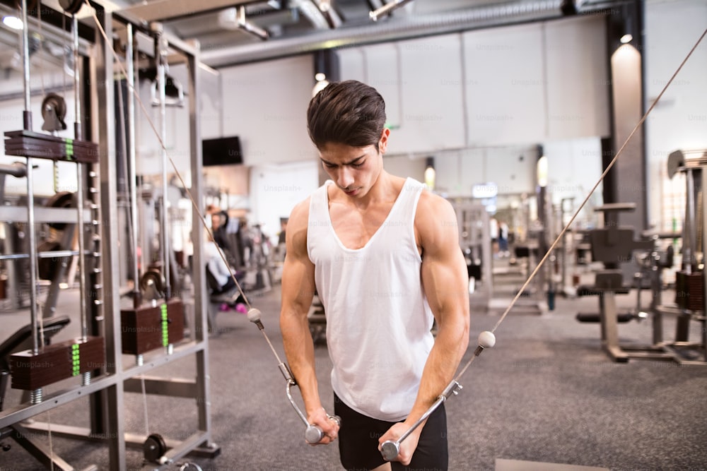 Joven culturista musculoso hispano haciendo ejercicio en el gimnasio en una máquina de cable, haciendo ejercicio de mosca de cable para una mejor definición de los músculos de sus brazos.