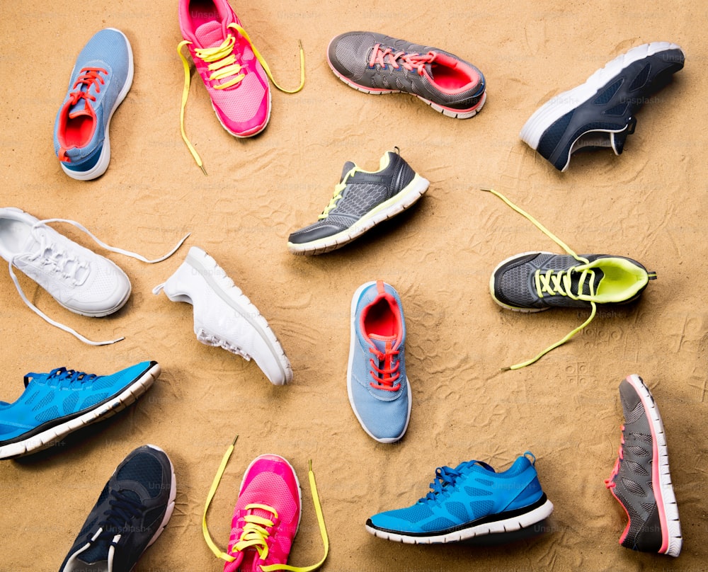 Various colorful sports shoes laid on sand beach background, studio shot, flat lay.