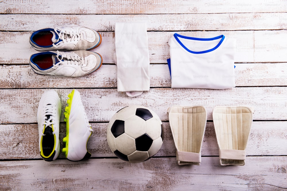 Soccer ball,cleats and various football stuff laid on wooden floor. Studio shot on white background. Flat lay, knolling.