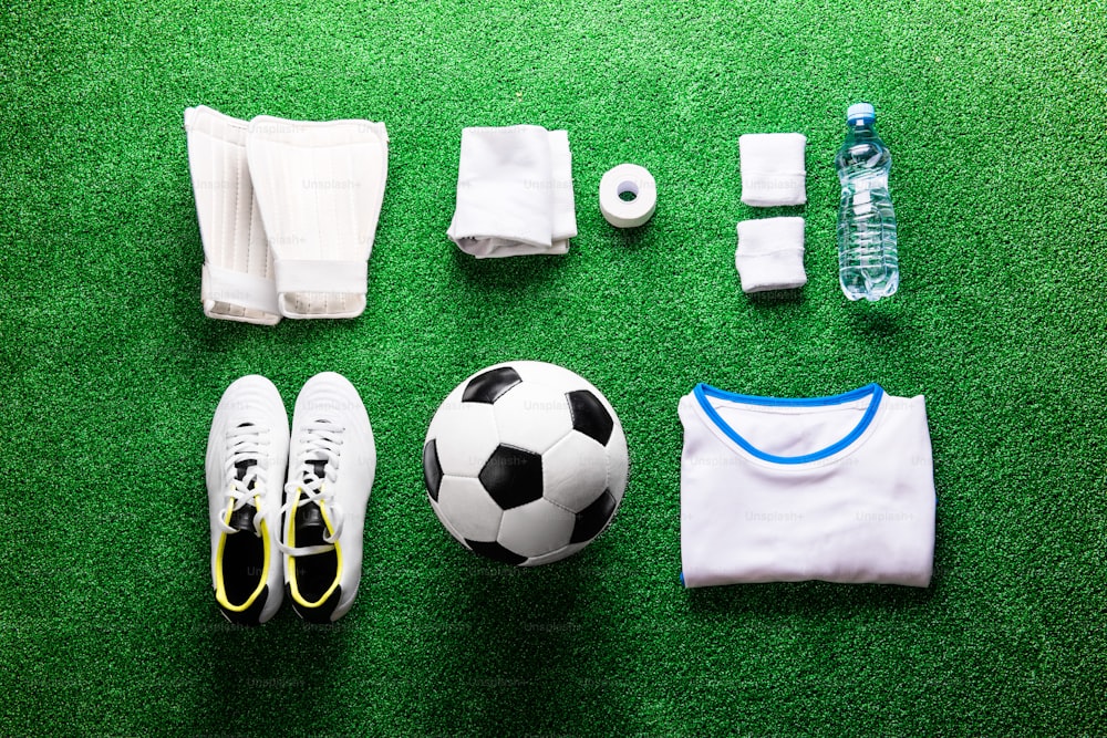 Soccer ball,cleats and various football stuff against artificial turf. Studio shot on green background. Flat lay, knolling.