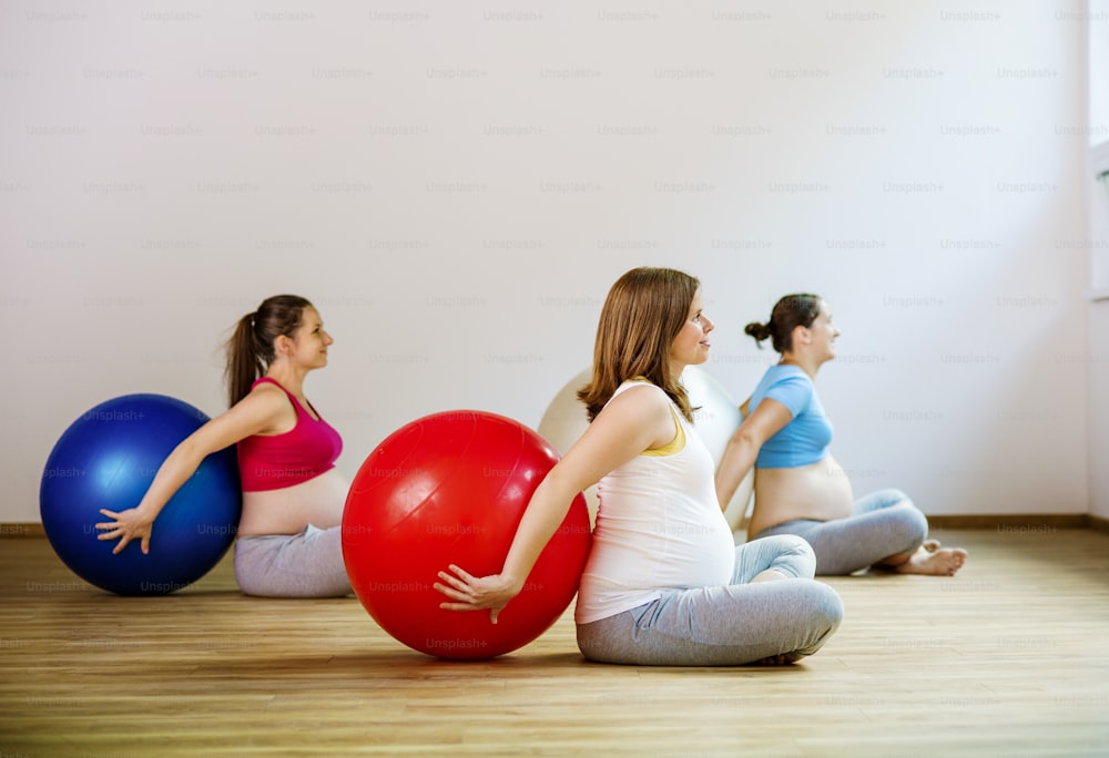 Mujeres embarazadas jóvenes haciendo ejercicio de relajación usando una pelota de fitness