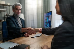 A financial advisor shaking hand with his client indoors in office.