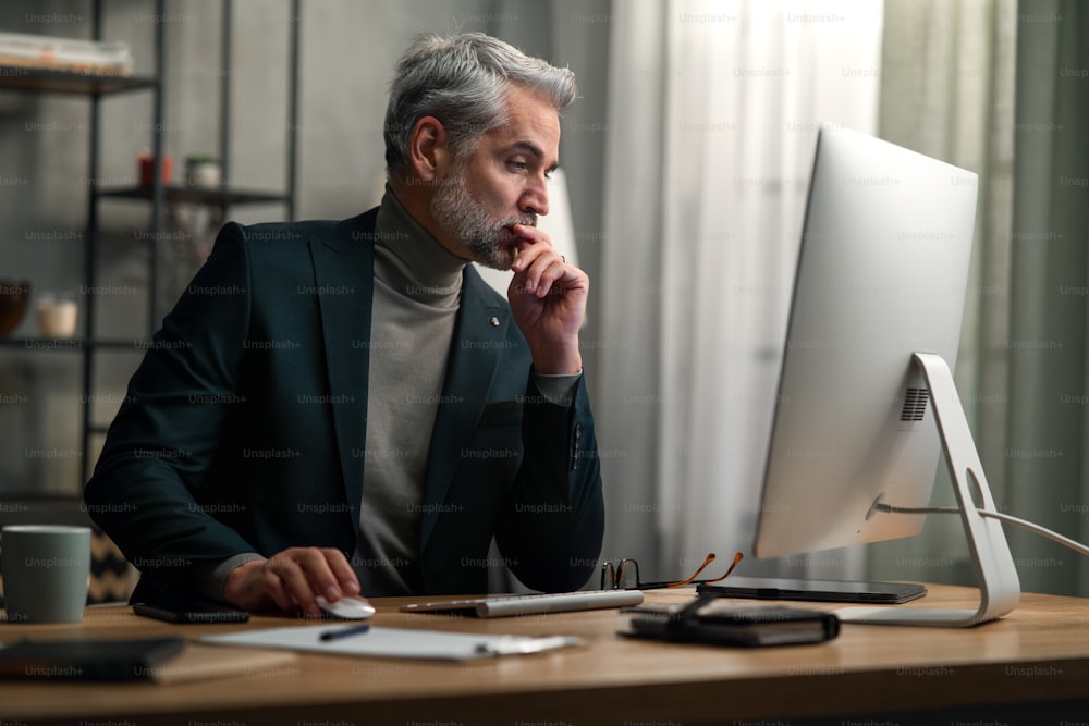 A mature businessman working on computer indoors in office.