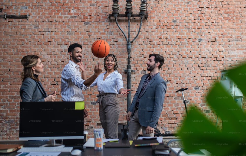 A group of cheerful young businesspeople playing basketball in office, taking a break.