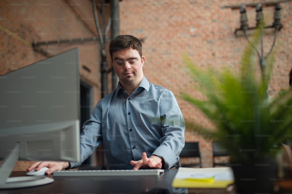 A happy down syndrome man working in office, social inclusion and cooperation concept.