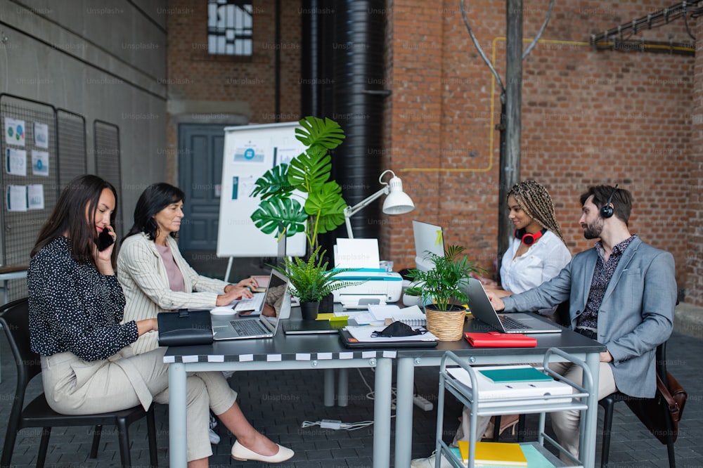 Young and old businesspeople sitting and working at desk in office, a cooperation and coworking concept.