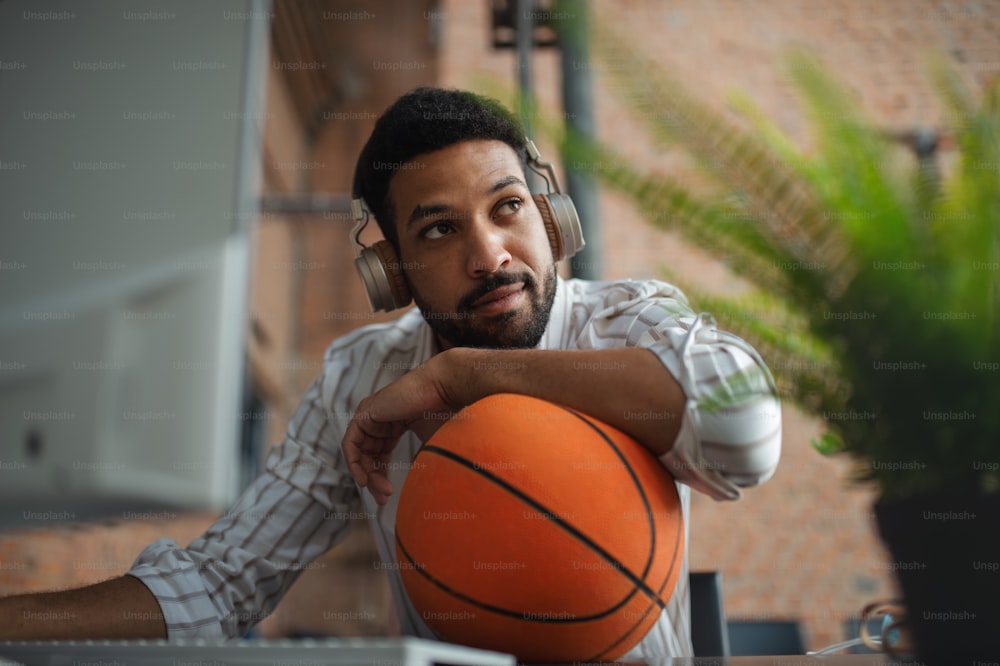 A cheerful young businessman with headphones and ball taking a break in office, resting.