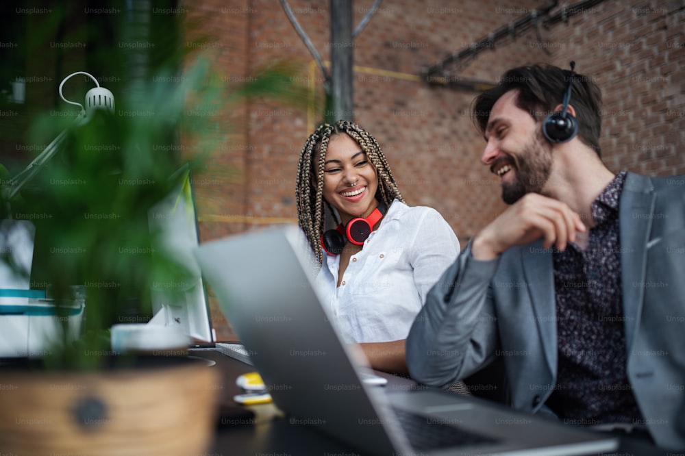 Cheerful young businesspeople sitting and working at desk in office, a cooperation concept.