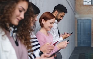 Seitenansicht einer Gruppe von Unternehmern, die im Büro mit dem Smartphone an einer Betonwand stehen.