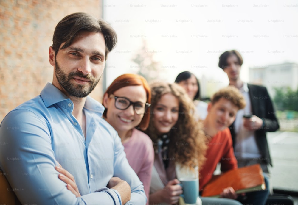 Ein Porträt eines jungen Geschäftsmannes mit einer Gruppe von Unternehmern im Büro, die in die Kamera schauen.