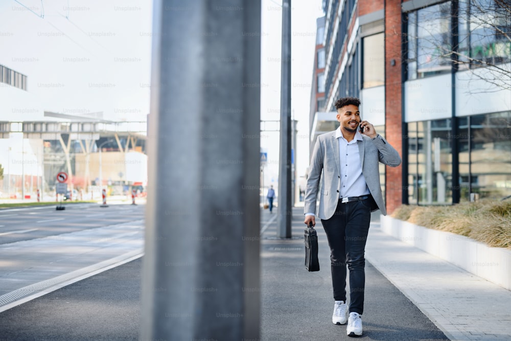A portrait of young man student walking outdoors on street in city, using smartphone.