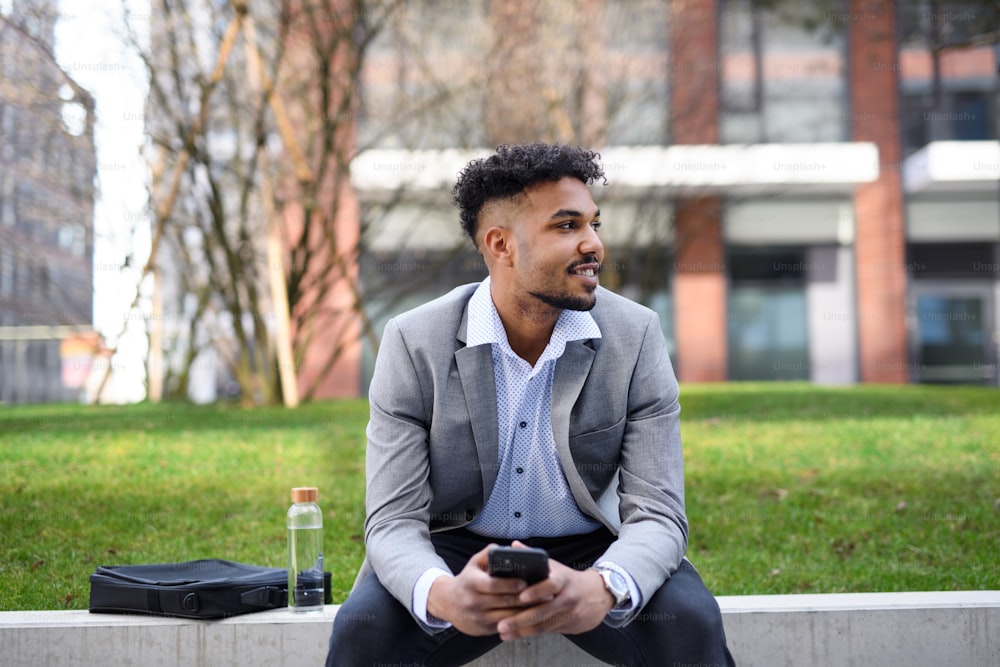 スマートフォンを使って、街の屋外に座っている若い男性の学生のポートレート。