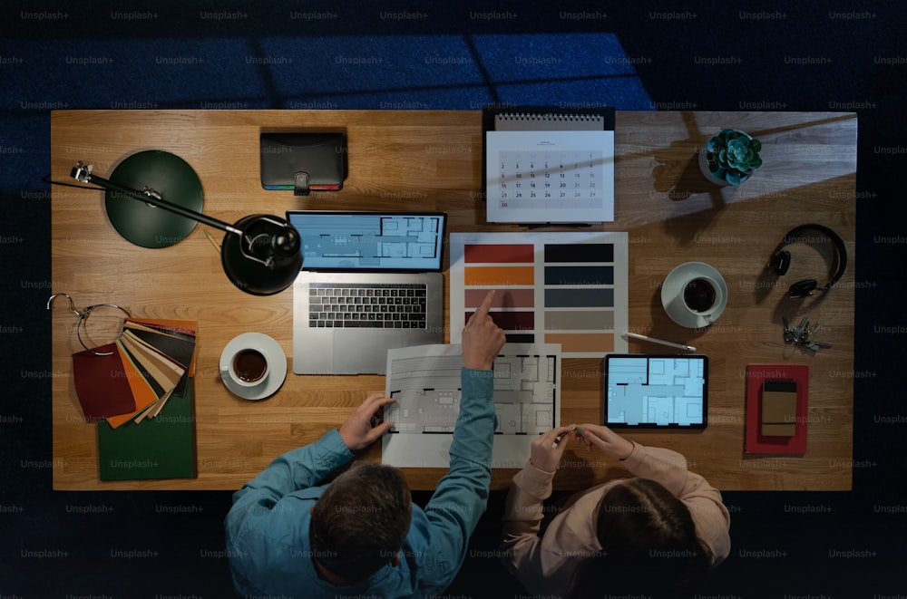 ホームオフィスで事務処理を行う机でコンピューターで作業している同僚の建築家の上面図。