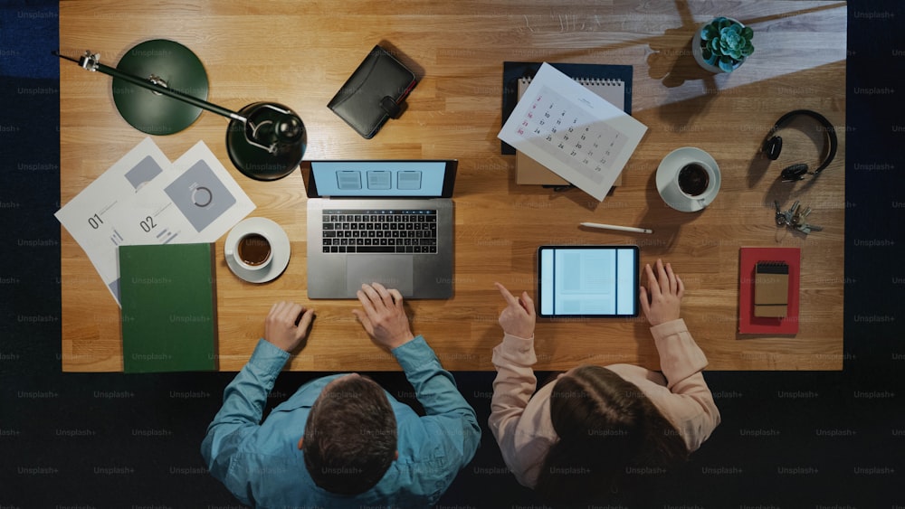 Vista superior de colegas empresários que trabalham no computador na mesa com papelada no escritório em casa.