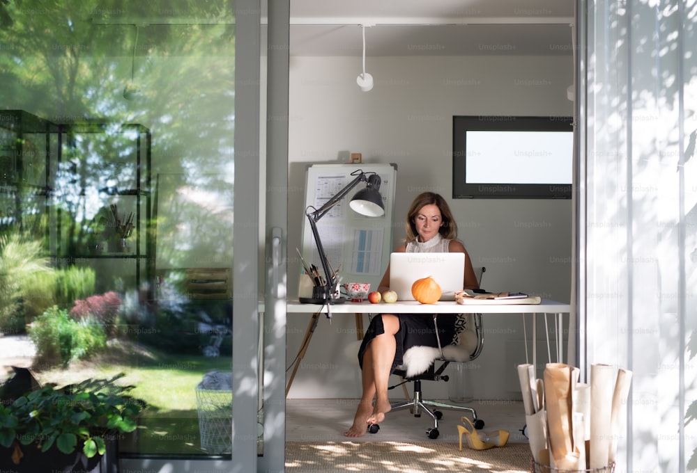 Vista frontal de una mujer madura que trabaja en el interior de la oficina en casa en la casa del contenedor en el patio trasero.