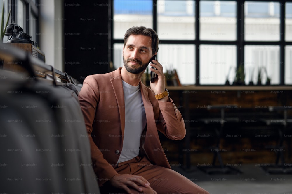 Portrait of young businessman with smartphone sitting indoors in office, looking at camera.