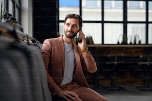 Portrait of young businessman with smartphone sitting indoors in office, looking at camera.