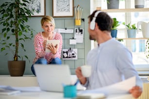 Mature businessman with headphones working and talking to colleague indoors in office.