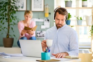 Vista frontal de un hombre de negocios maduro con auriculares y computadora portátil en el interior de la oficina en casa, trabajando.