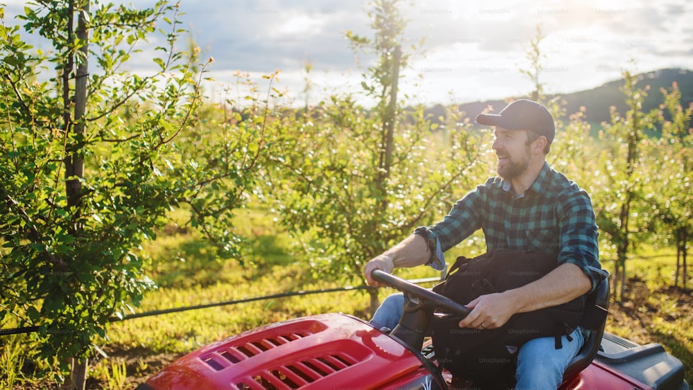 Eine Vorderansicht eines reifen Landwirts, der einen Minitraktor im Freien im Obstgarten fährt.