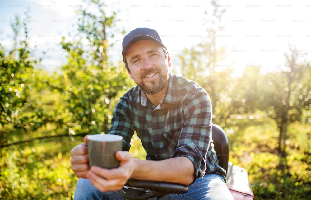 果樹園で屋外でコーヒーを飲み、休んでいる成熟した農家の正面図。