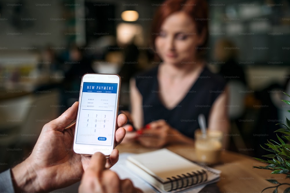 Meio-fio de empresários irreconhecíveis com smartphone em um café, verificando as finanças.