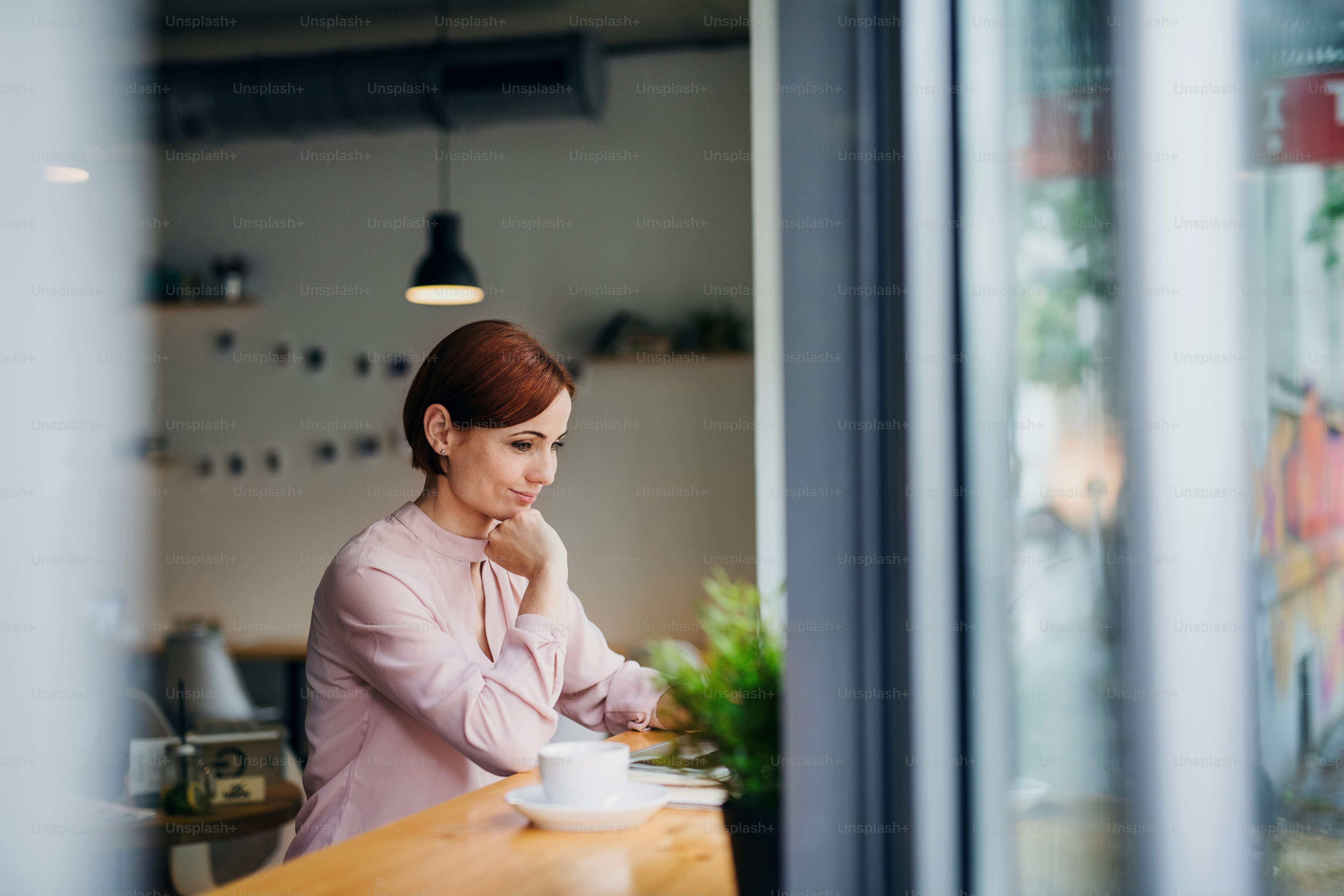 A portrait of attractive woman with coffee sitting at the table in a cafe, using laptop.