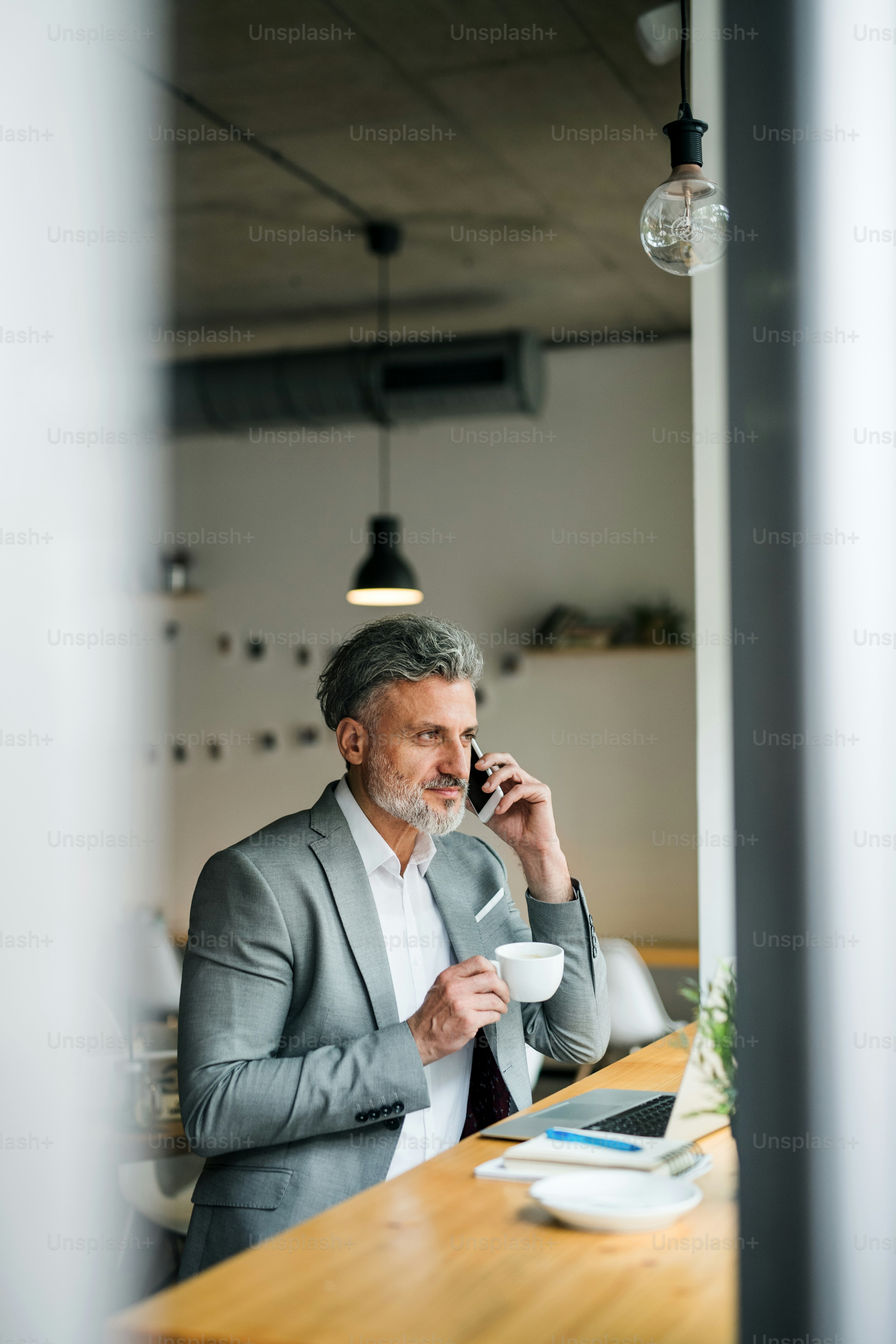 A mature man with coffee and smartphone at the table in a cafe, making a phone call.