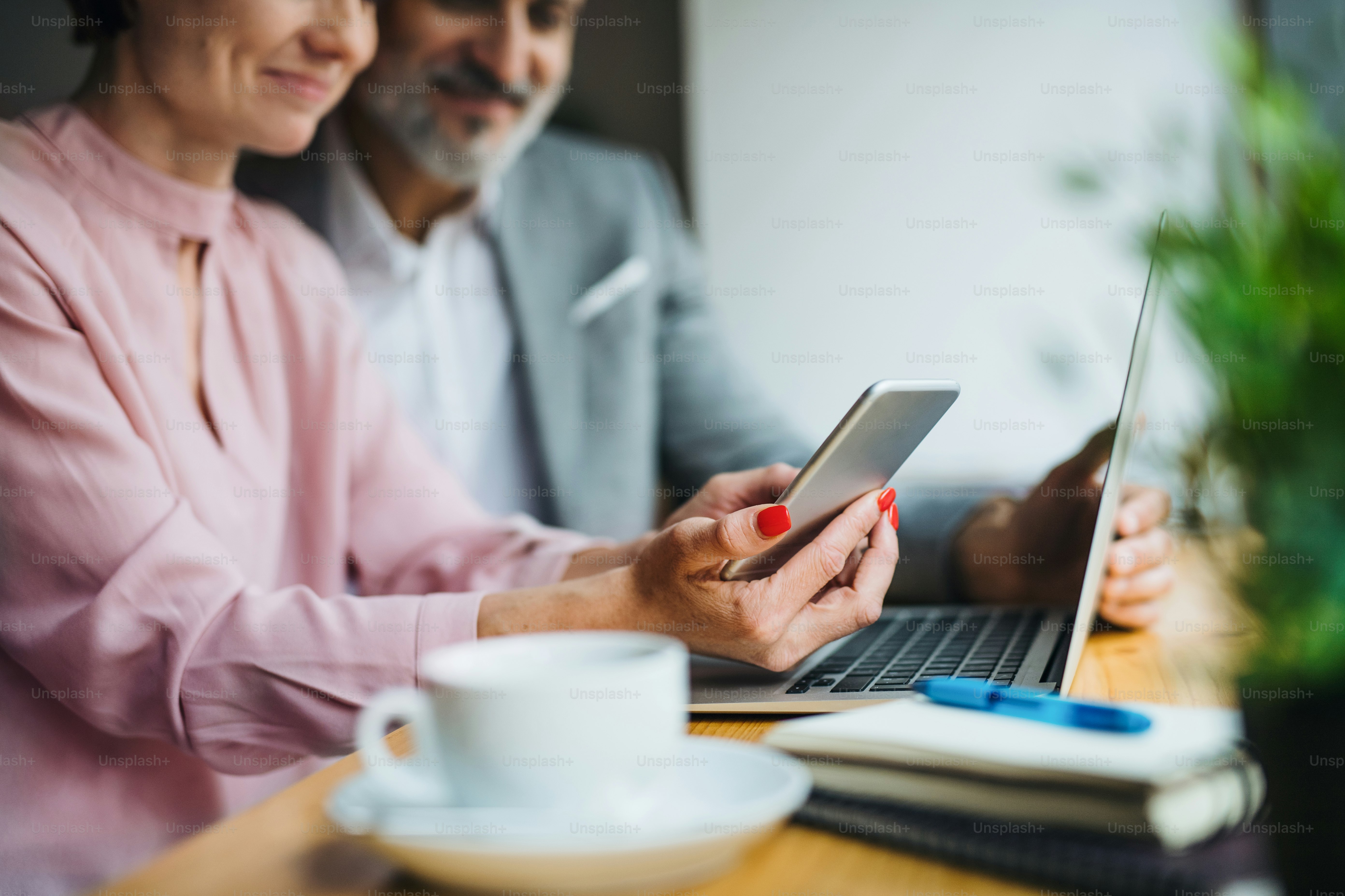 A midsection of man and woman having business meeting in a cafe, using laptop and smartphone.