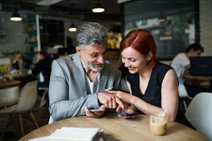 Un homme et une femme avec un café se rencontrant dans un café, à l’aide d’un smartphone.