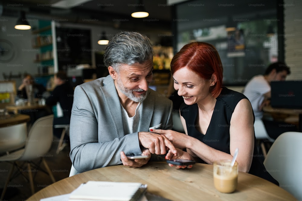 Un hombre y una mujer con café teniendo una reunión de negocios en una cafetería, usando un teléfono inteligente.