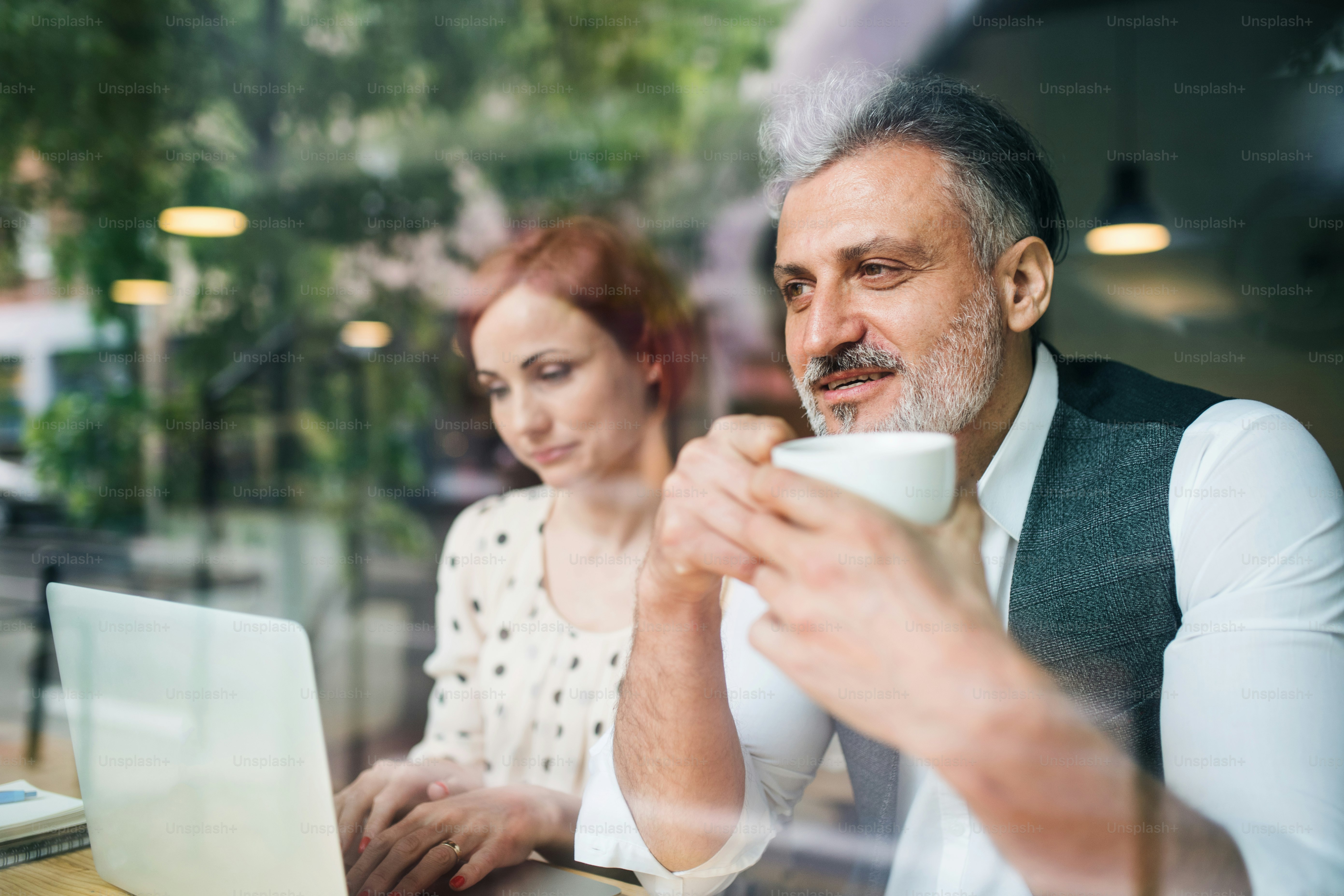 A man and woman having business meeting in a cafe, using laptop. Shot through glass.