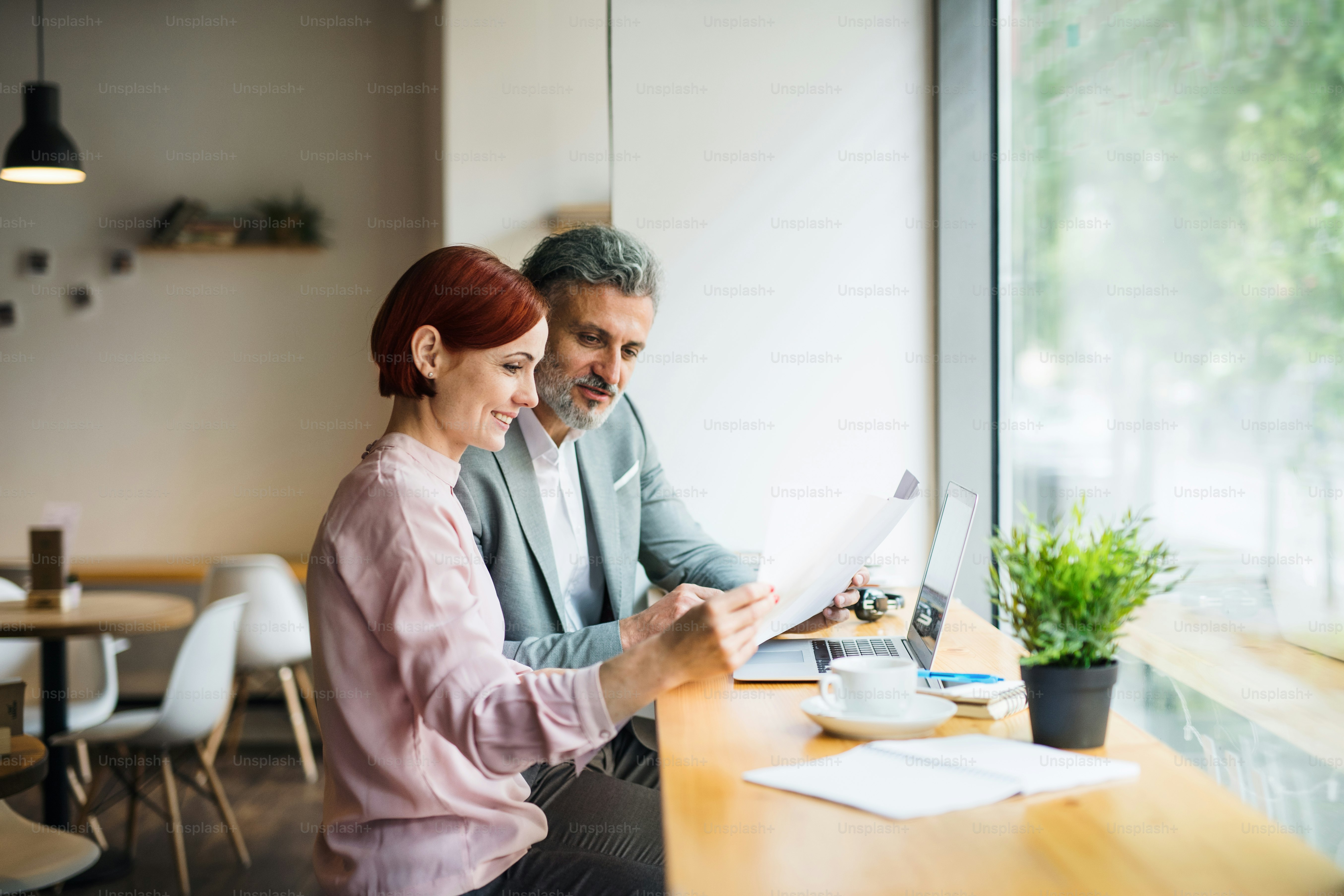 A man and woman having business meeting in a cafe, looking at blueprints.
