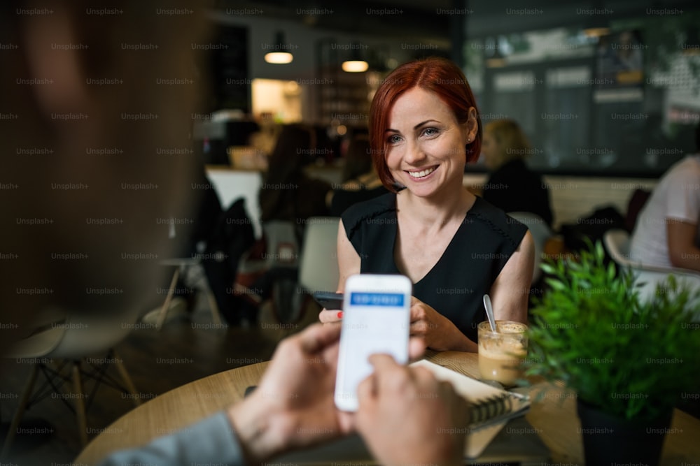 Sección media de empresarios irreconocibles con teléfonos inteligentes en un café, revisando finanzas.