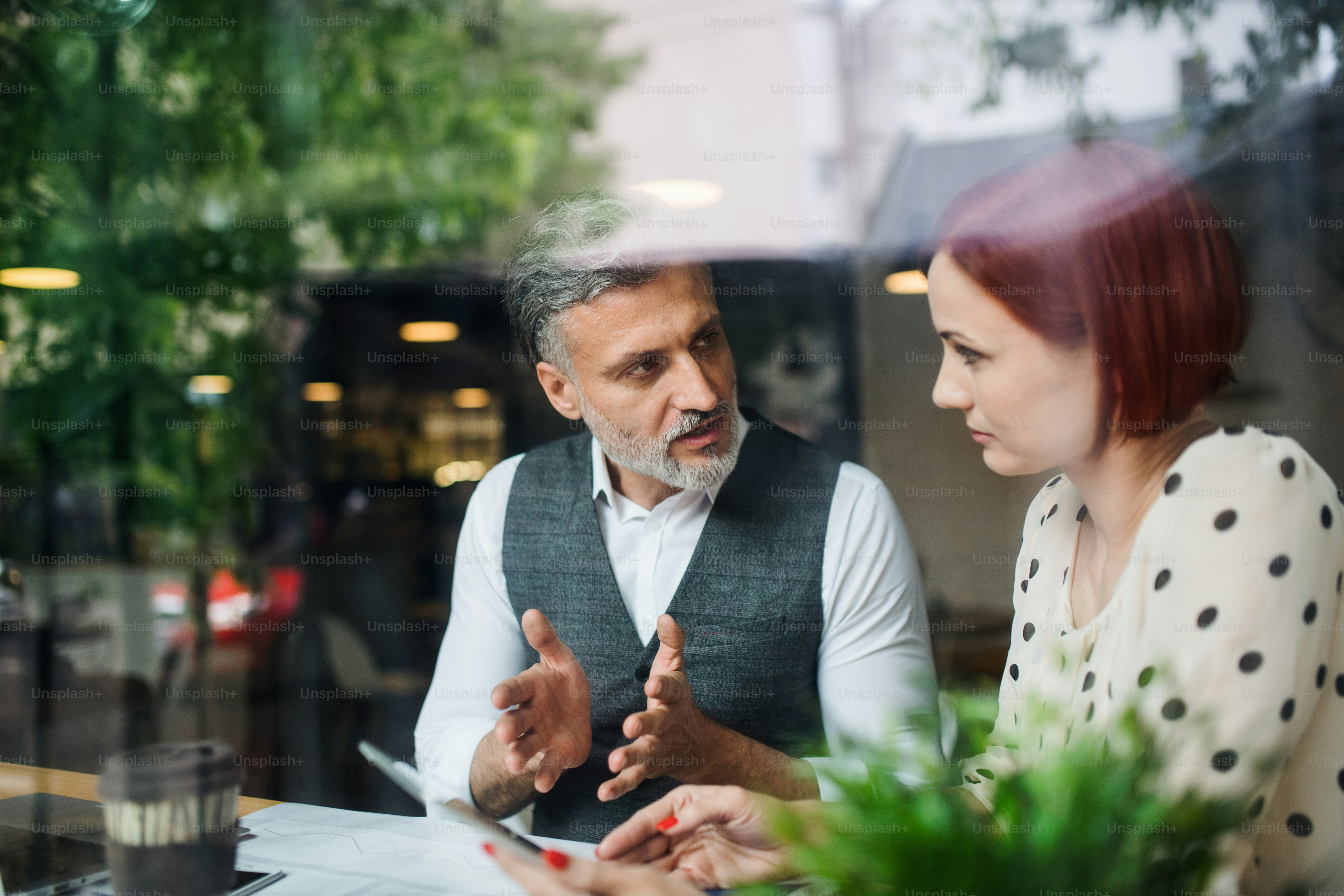 A man and woman having business meeting in a cafe, using tablet. Shot through glass.