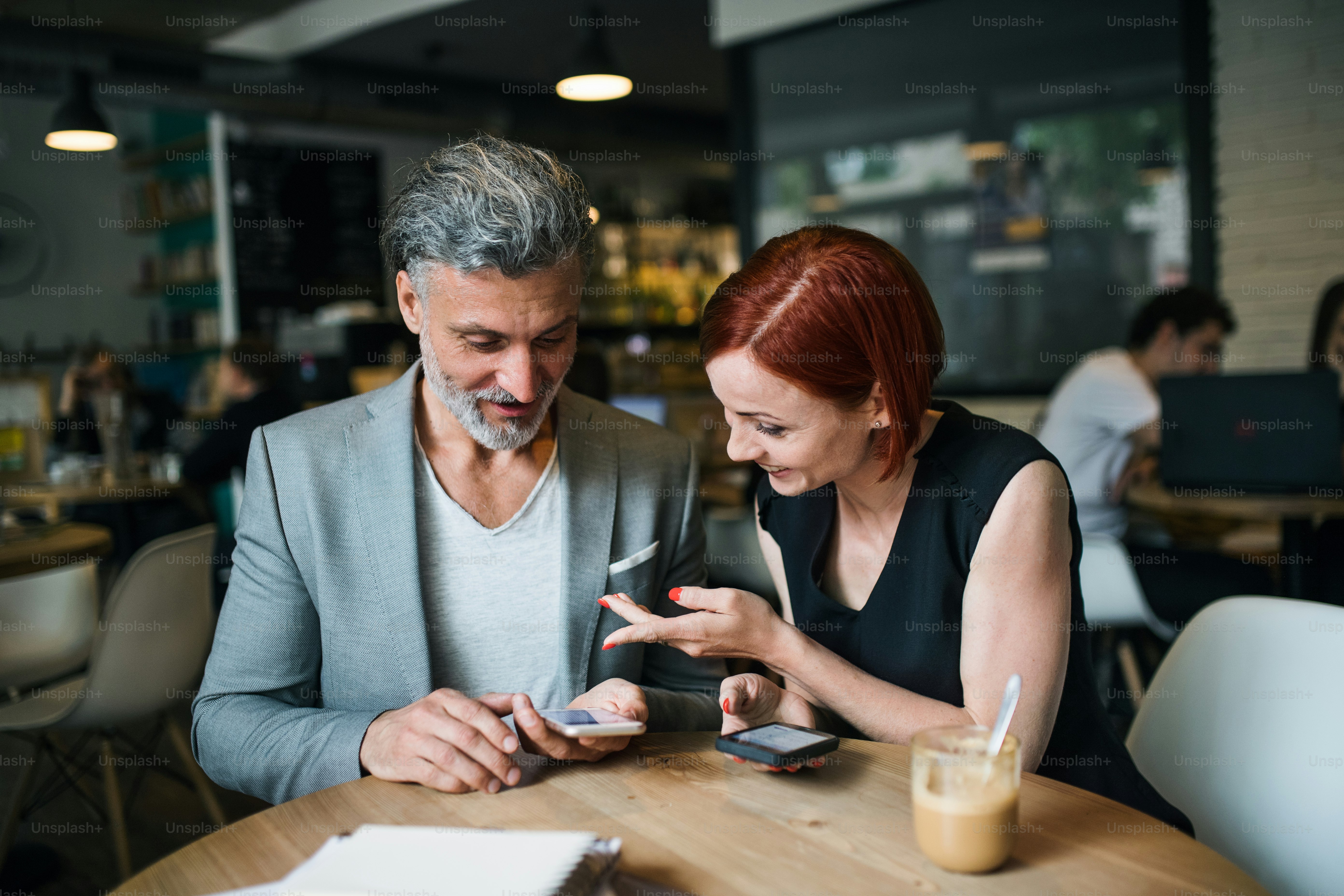 A man and woman with coffee having business meeting in a cafe, using smartphone.
