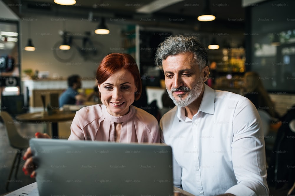 Un hombre y una mujer teniendo una reunión de negocios en un café, usando una computadora portátil.