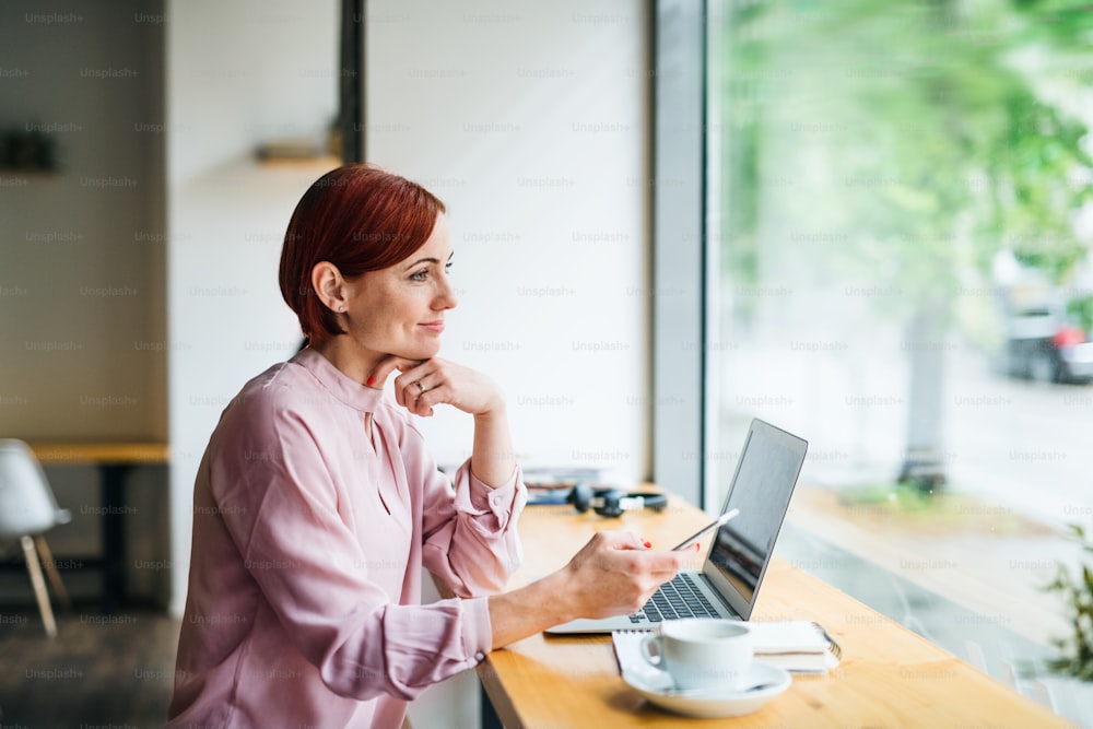 An attractive woman with coffee, laptop and telephone sitting at the table in a cafe.