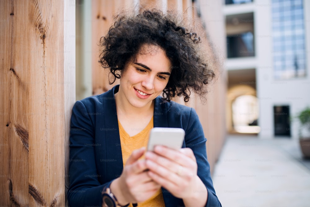 Uma jovem empresária feliz com smartphone ao ar livre, mensagens de texto. Conceito de start-up.
