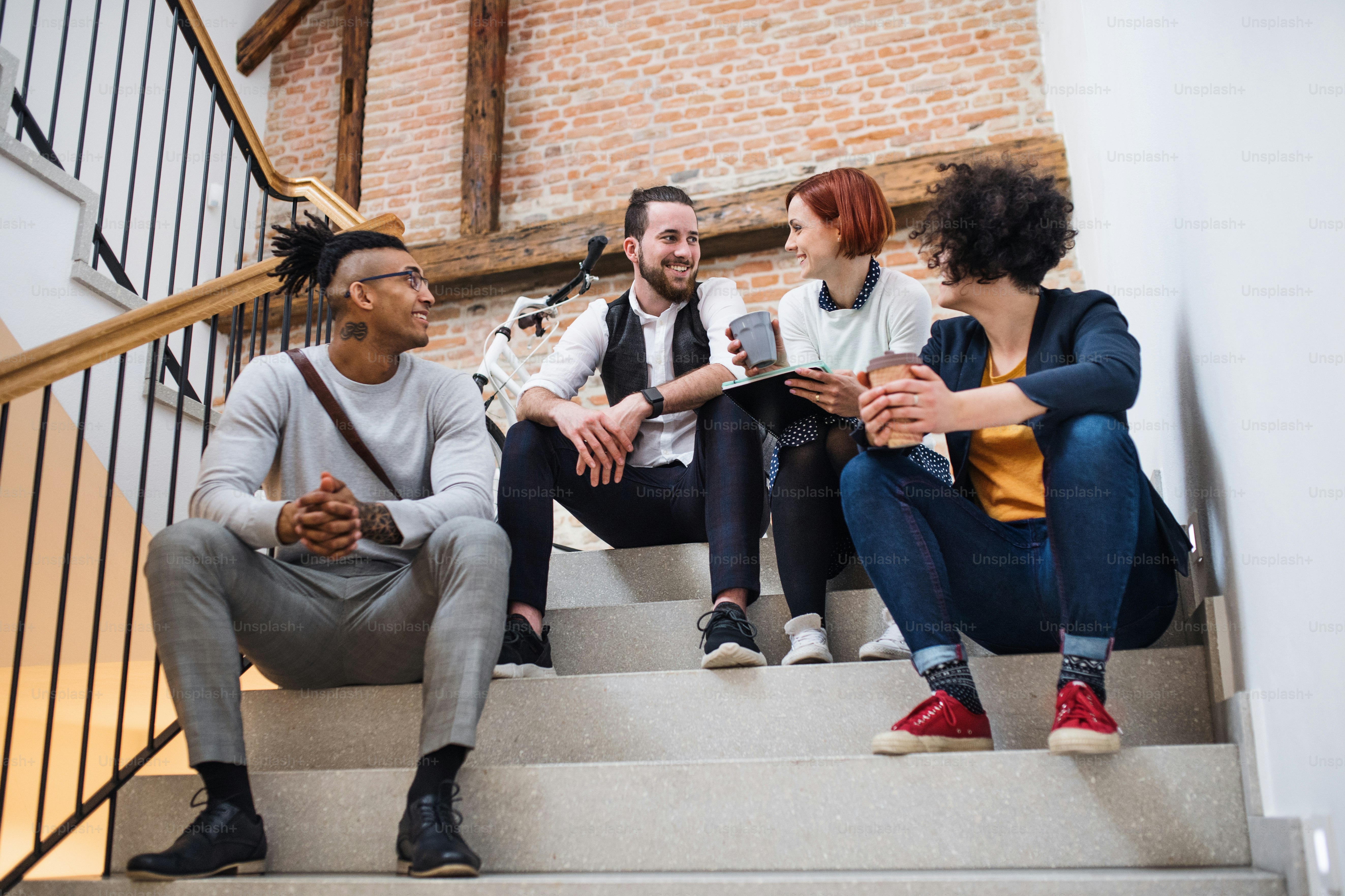 Grupo de jóvenes empresarios sentados en escaleras adentro, hablando. Un concepto de start-up