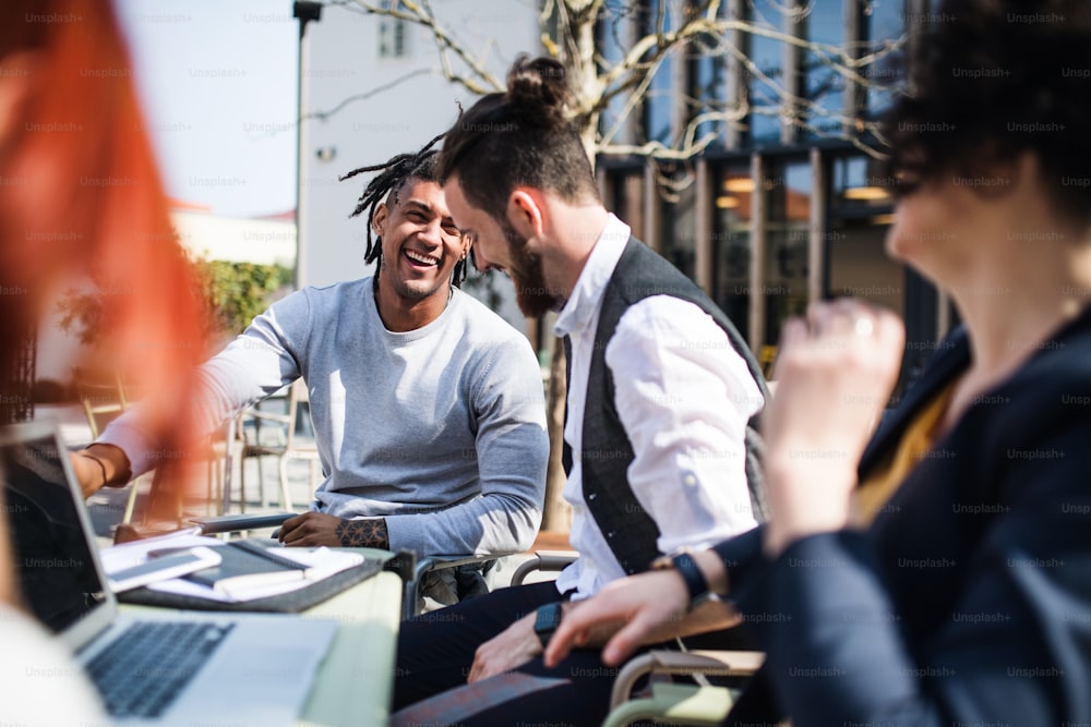 Giovani uomini d'affari con computer portatile all'aperto nel cortile, ridendo. Concetto di start-up.