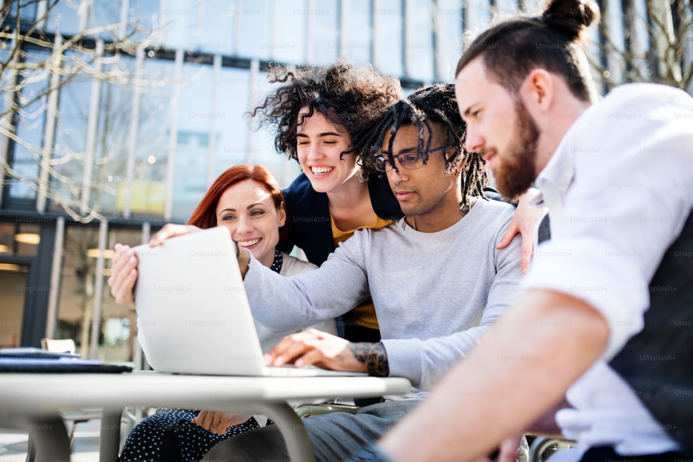 Giovani uomini d'affari con computer portatile all'aperto nel cortile, ridendo. Concetto di start-up.