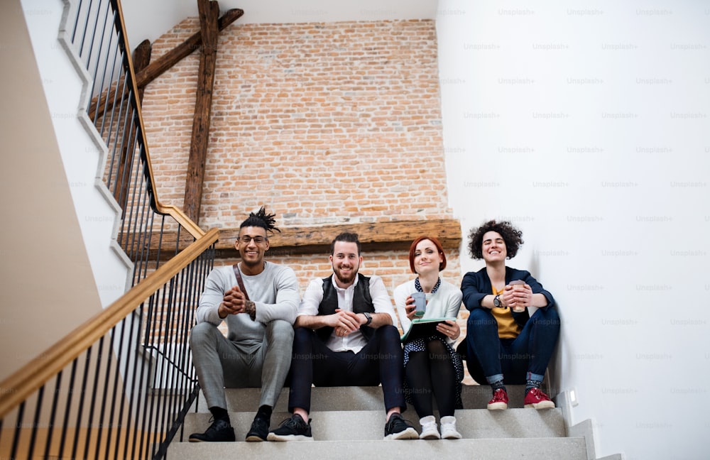 Grupo de jovens empresários sentados em escadas dentro de casa, olhando para a câmera. Um conceito de start-up.