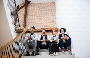 Group of young businesspeople sitting on stairs indoors, looking at camera. A start-up concept.