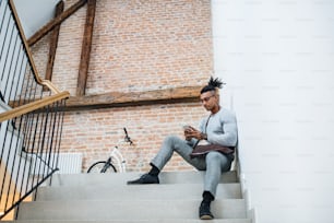 Un giovane uomo d'affari di razza mista con il telefono seduto sulle scale in un edificio per uffici.