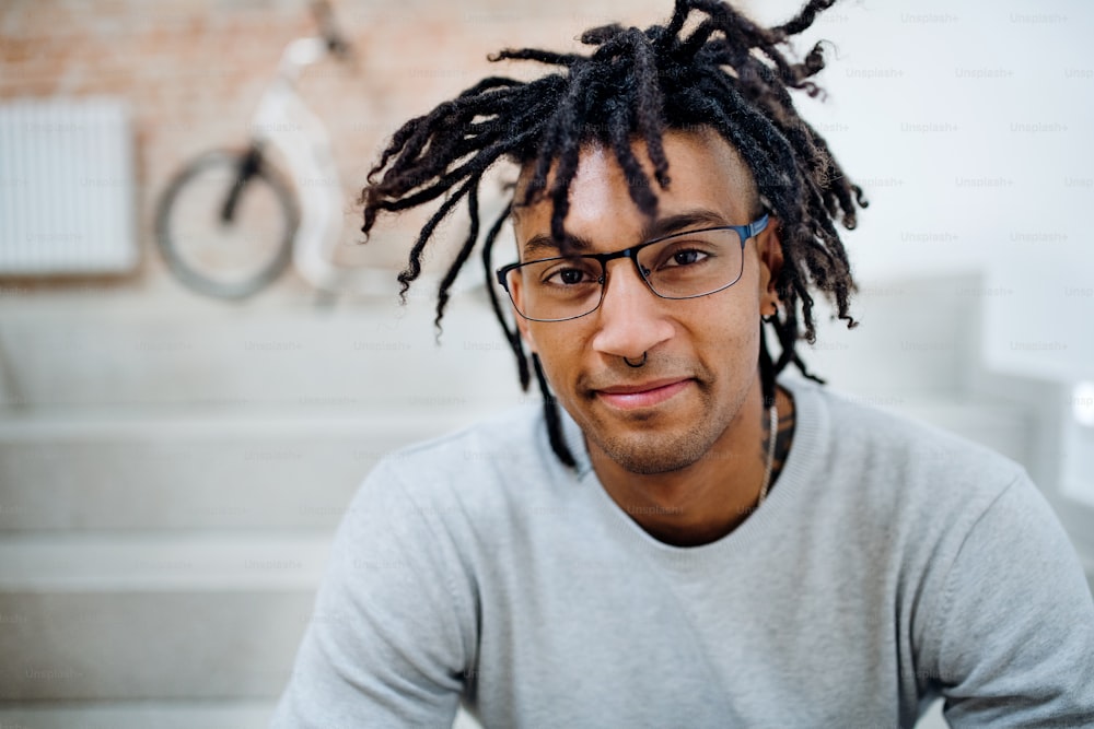A portrait of young mixed race businessman with dreadlocks in office, looking at camera.