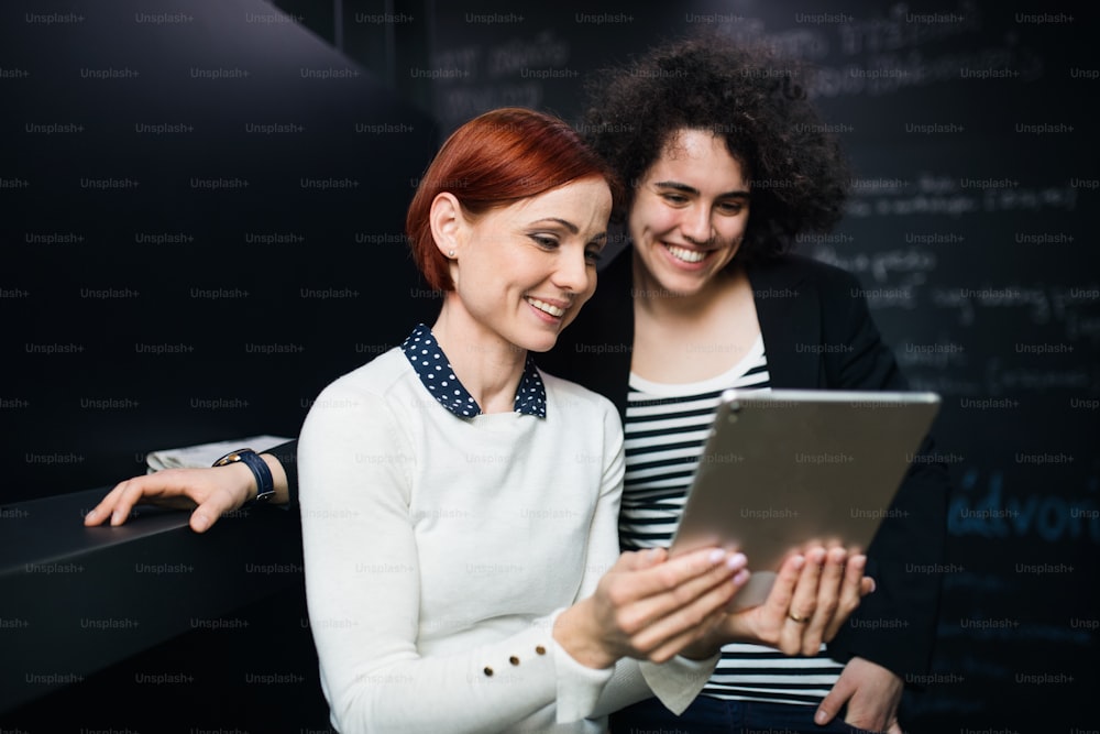 Two young cheerful female businesspeople using tablet in office, start-up concept.